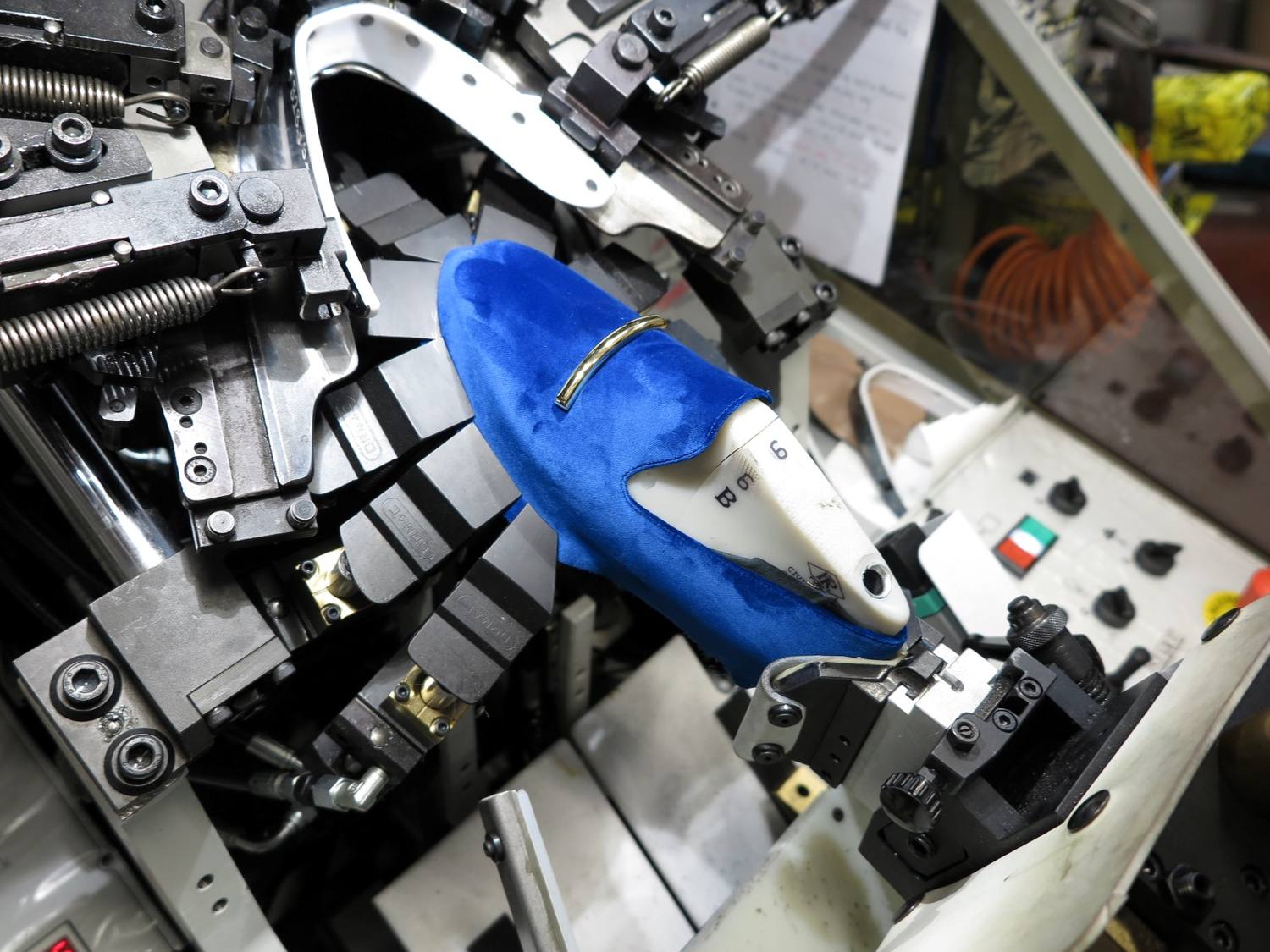 Close-up of an automated toe lasting machine stretching a blue velvet shoe upper over a white last.